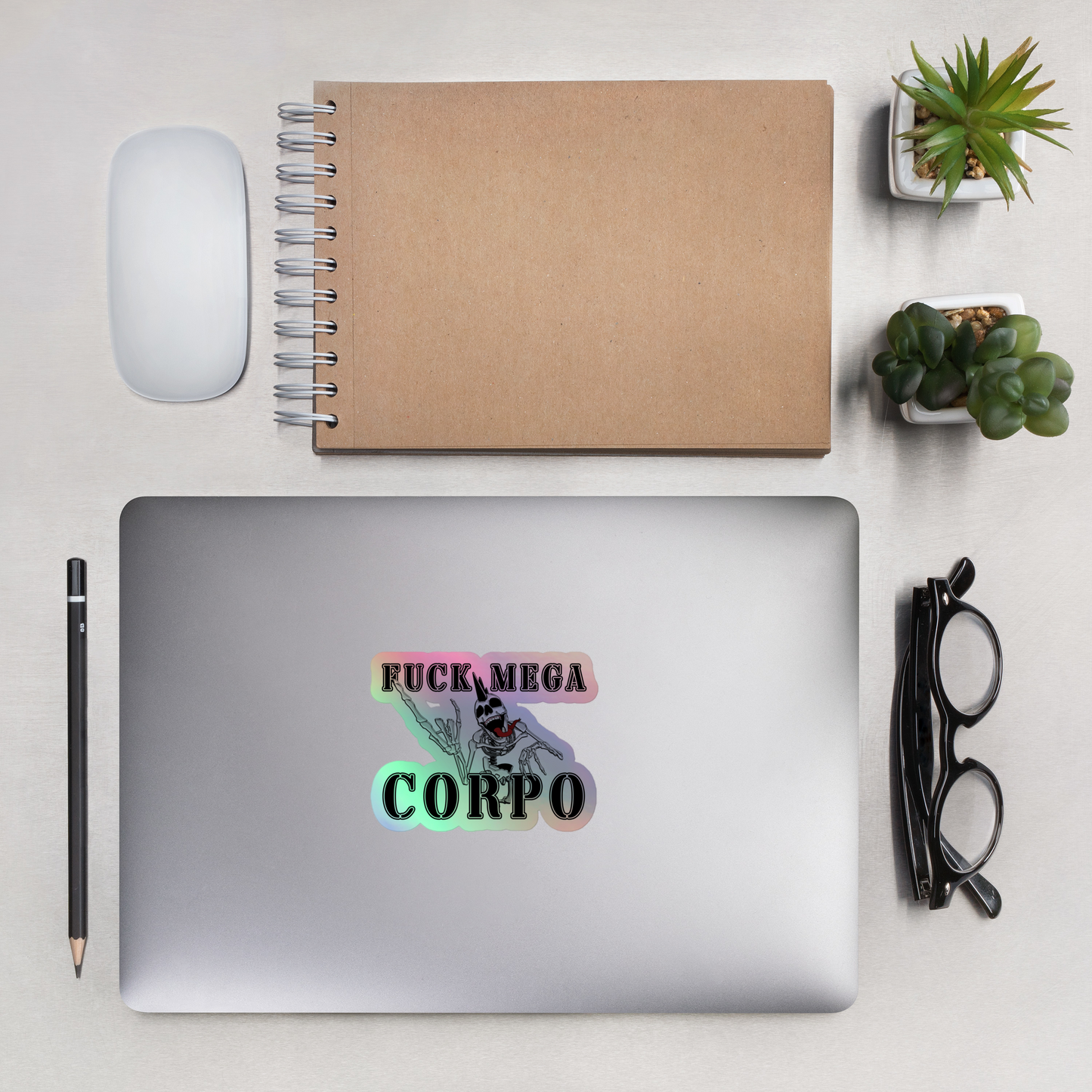 Laptop with a sticker on a desk with a notebook, mouse, pencil, and glasses.