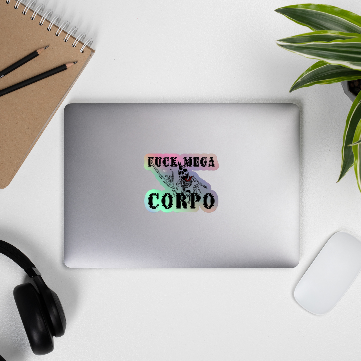 Laptop with a sticker on a desk with a notebook, pencils, headphones, and a plant.