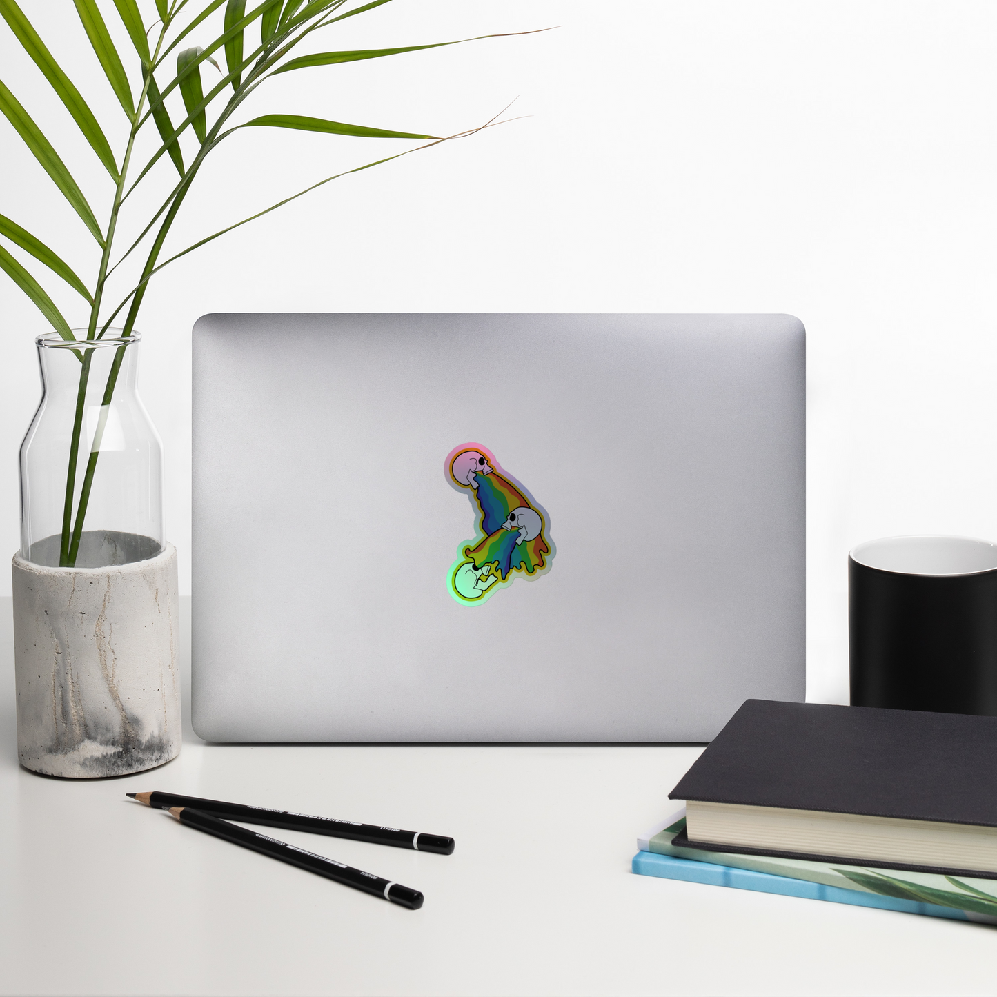 Laptop with a colorful holographic rainbow sticker on a desk with a plant, pencils, and books