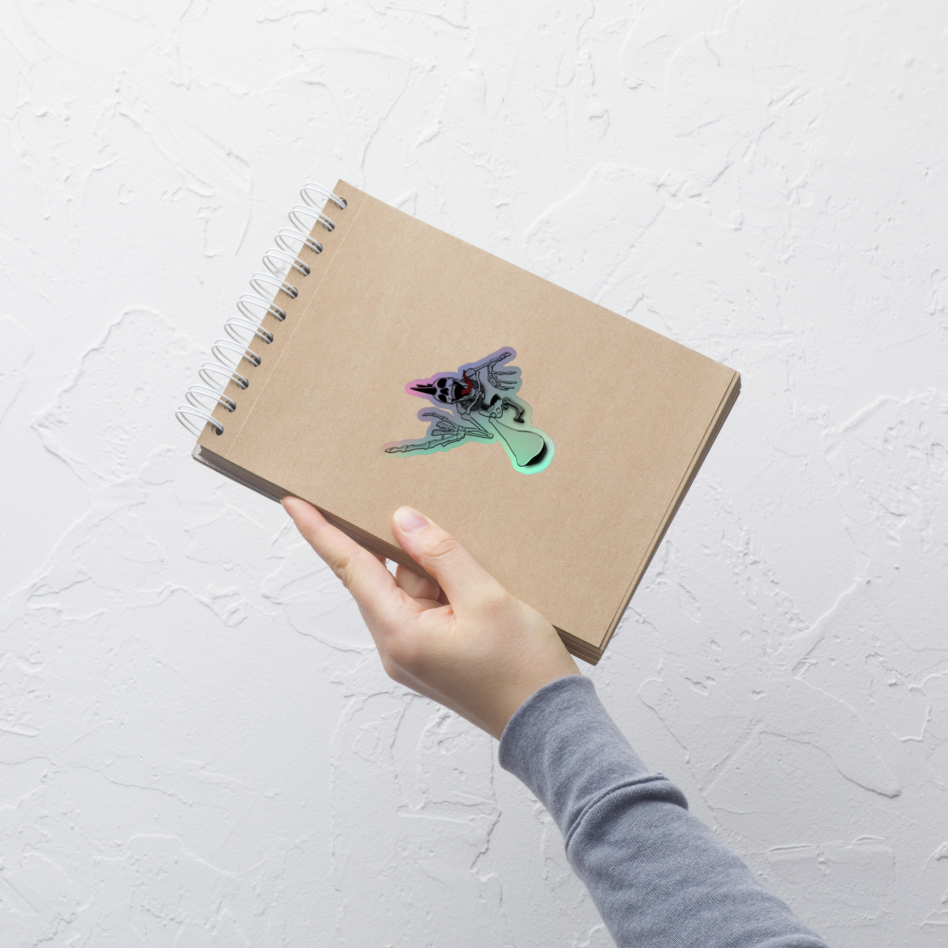 Hand holding a brown notebook with a holographic sticker on a light gray background