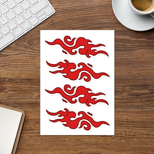 A sheet of four red flame-shaped decals or stickers on a white backing, placed on a wooden desk with a keyboard, coffee cup, and notebook partially visible around it.