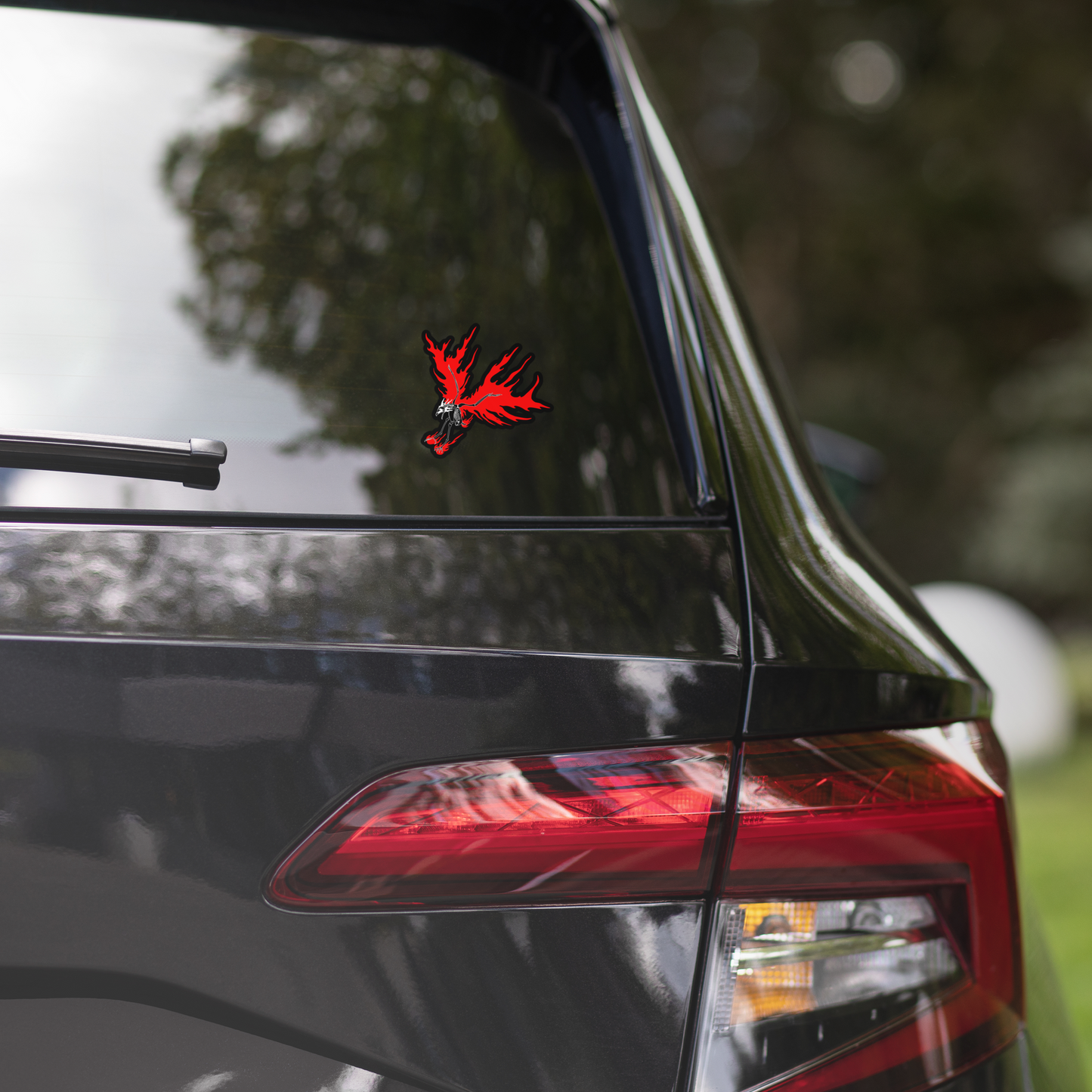 Car's rear window with a red and black decal, blurred greenery in the background