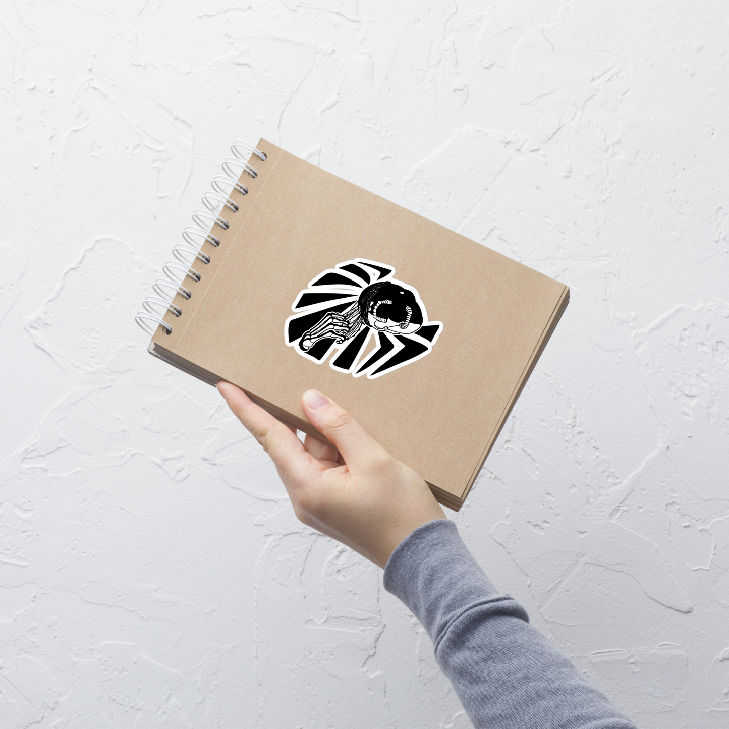 Hand holding a brown notebook with a black and white design on a light gray background
