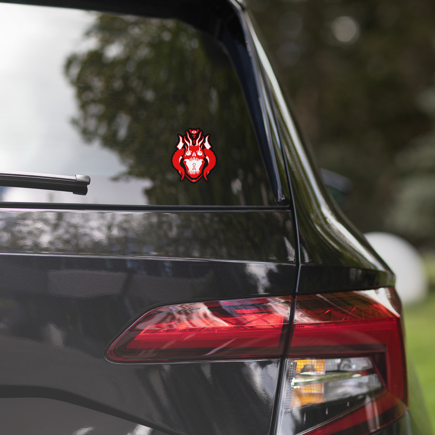 Car with a red and black decal on the back window, surrounded by trees.