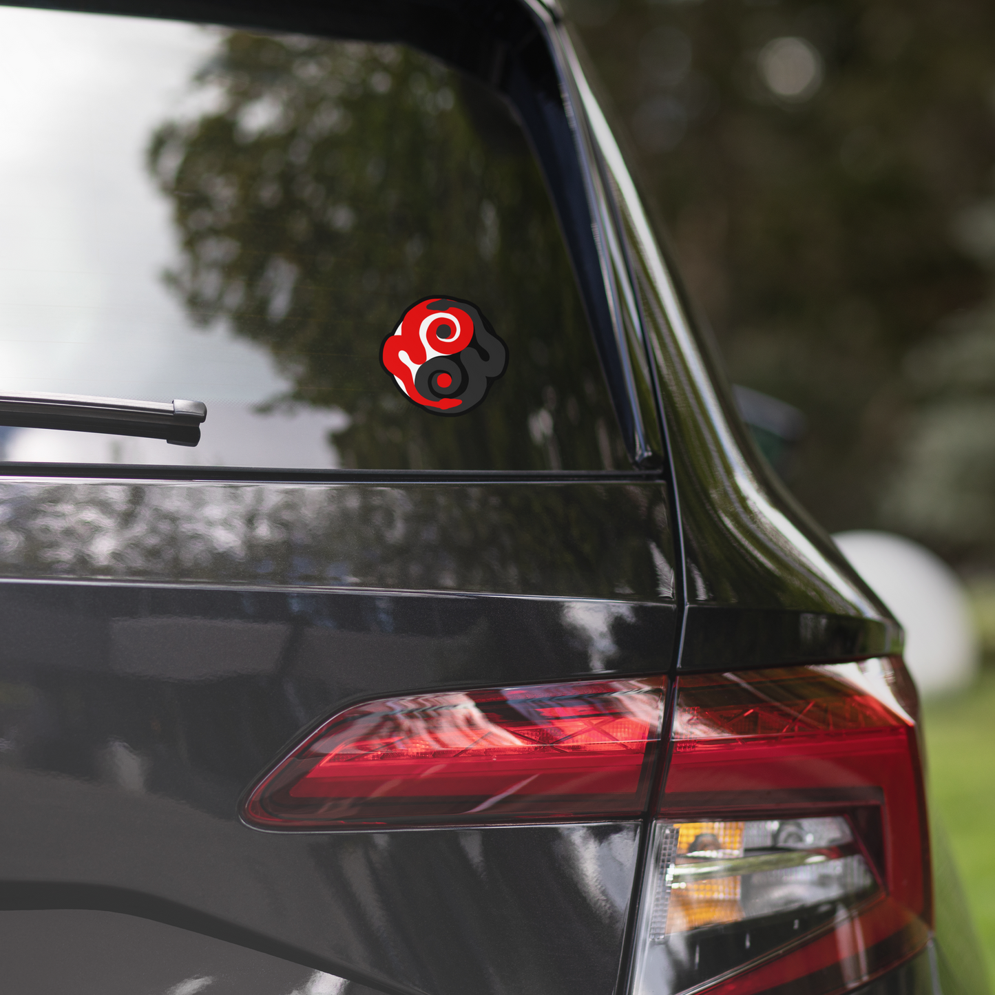 Car with a red and black circular decal on the back window, blurred greenery in the background