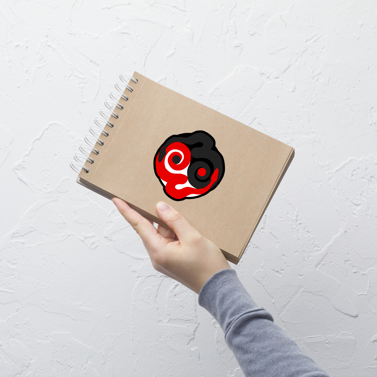 Notebook with a black and red design held by a hand on a light gray background