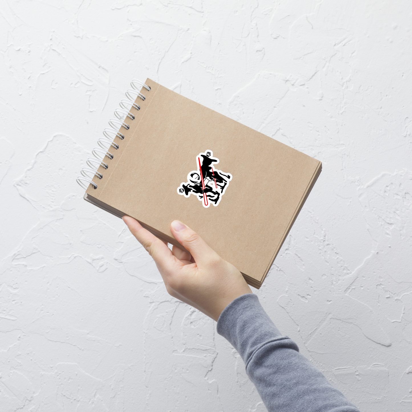 Hand holding a brown notebook with a sticker on a light gray background