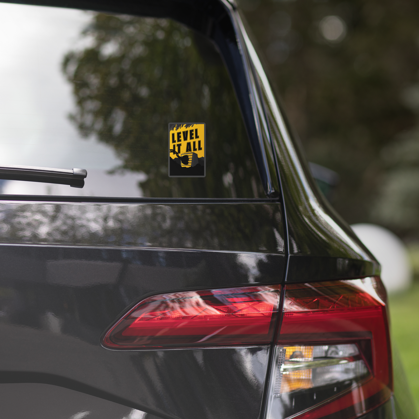 Car with a 'Level It All' decal on the rear window, blurred greenery in the background