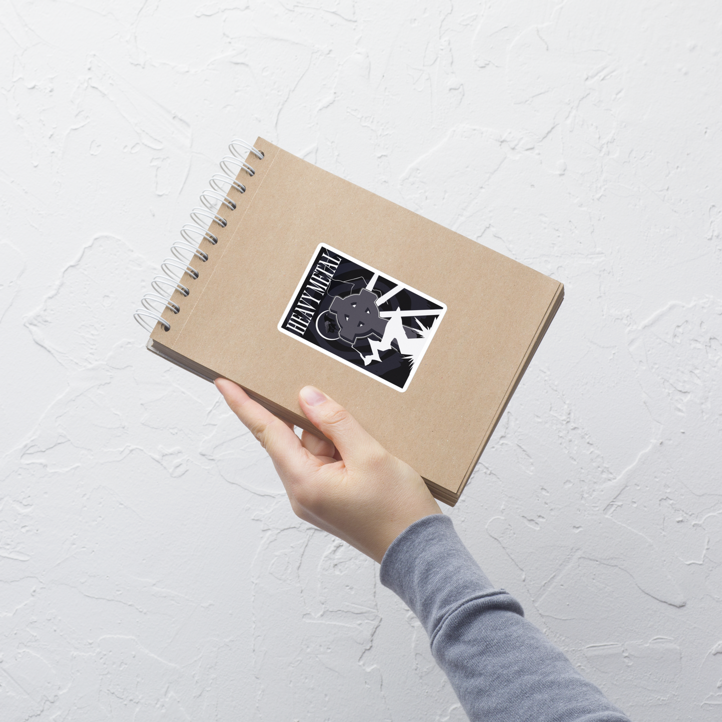 Hand holding a brown notebook with a logo on a light gray background
