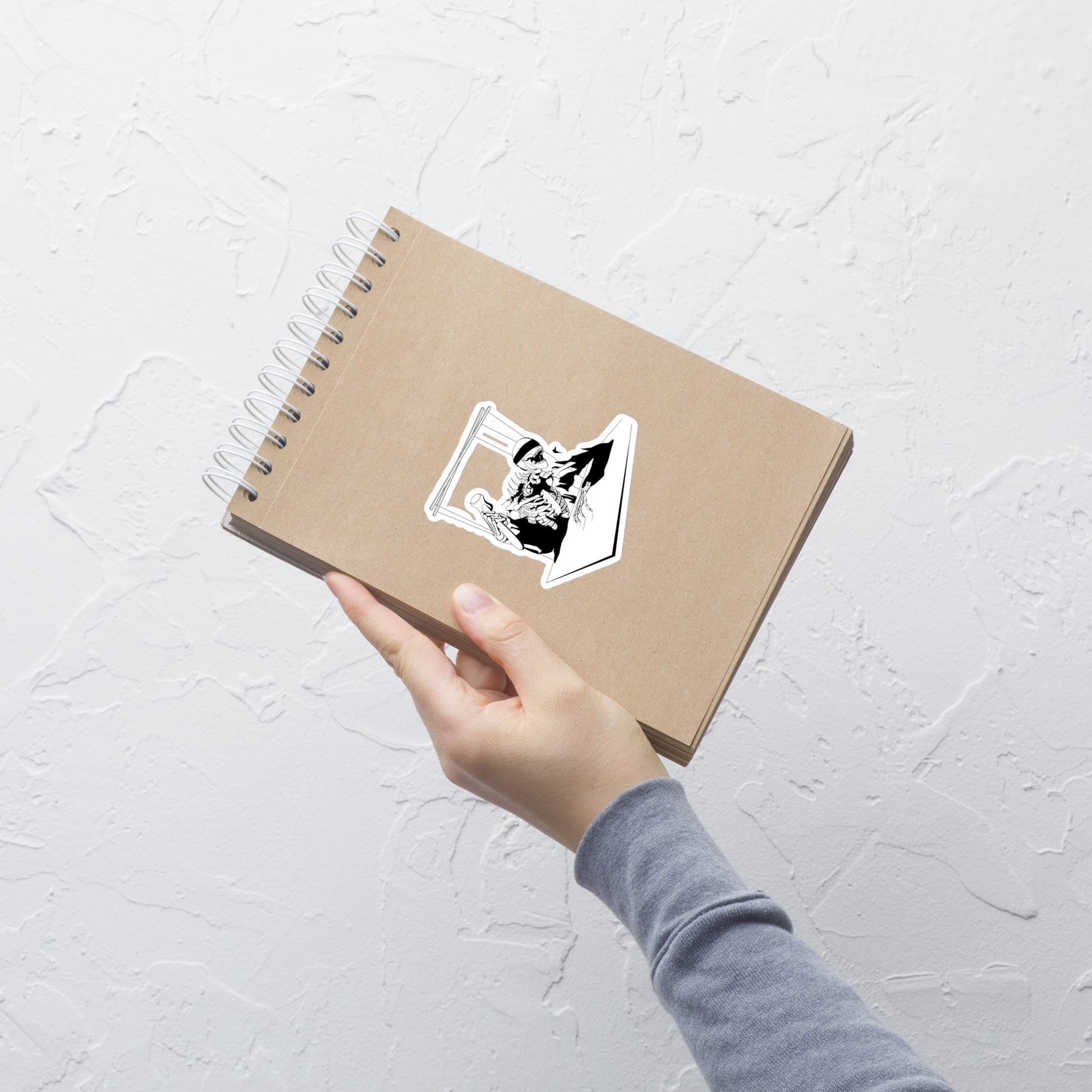 Hand holding a brown notebook with a sticker on a light gray textured background
