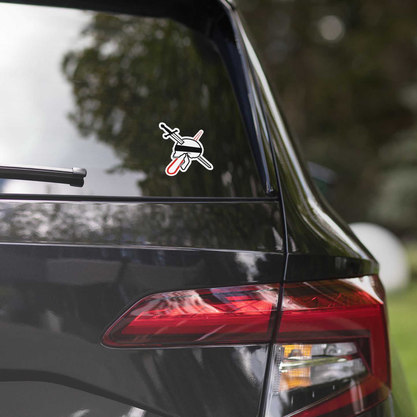 Car with a neorebellion logo sticker with no text on the rear window, blurred greenery in the background