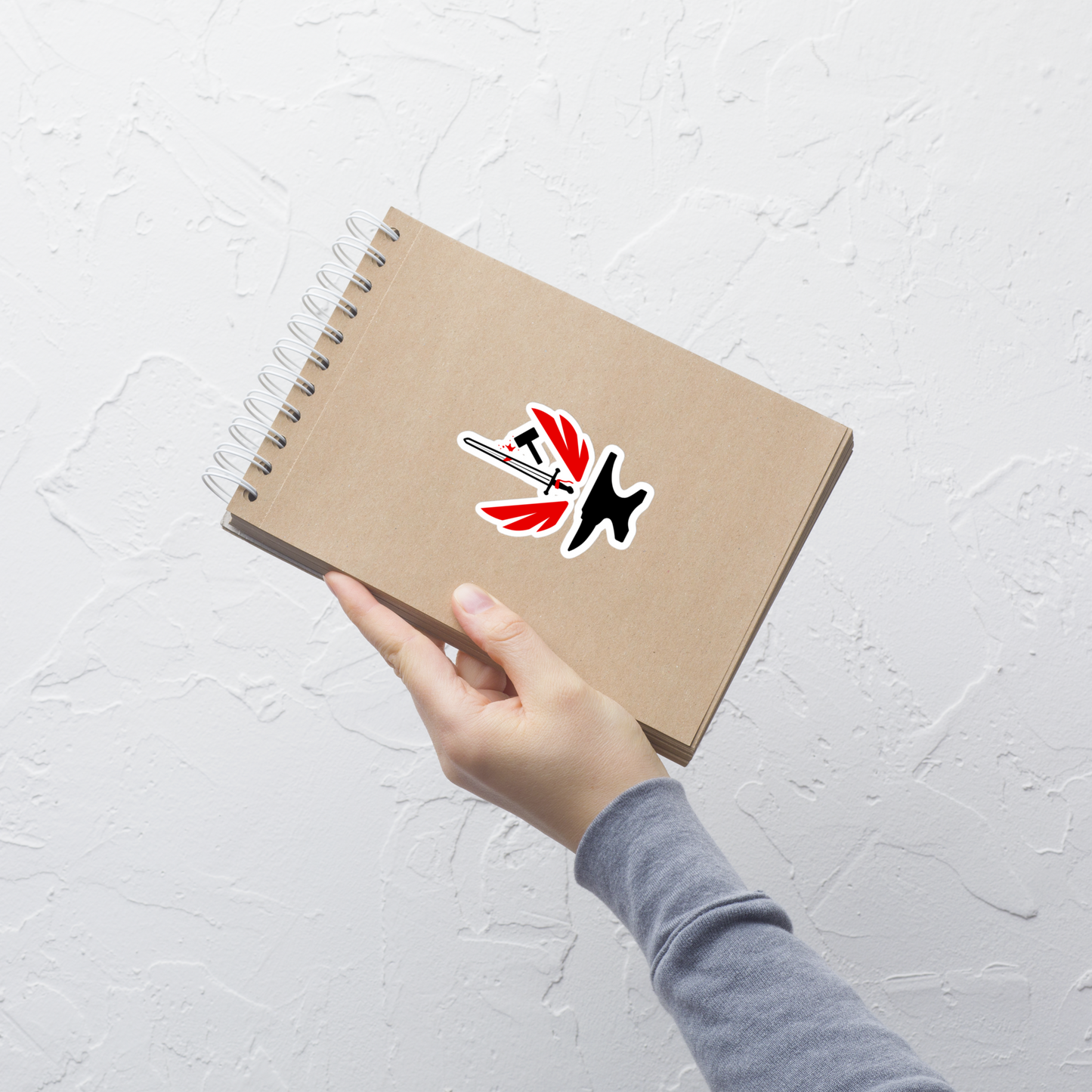 Hand holding a brown notebook with a logo on a light gray background