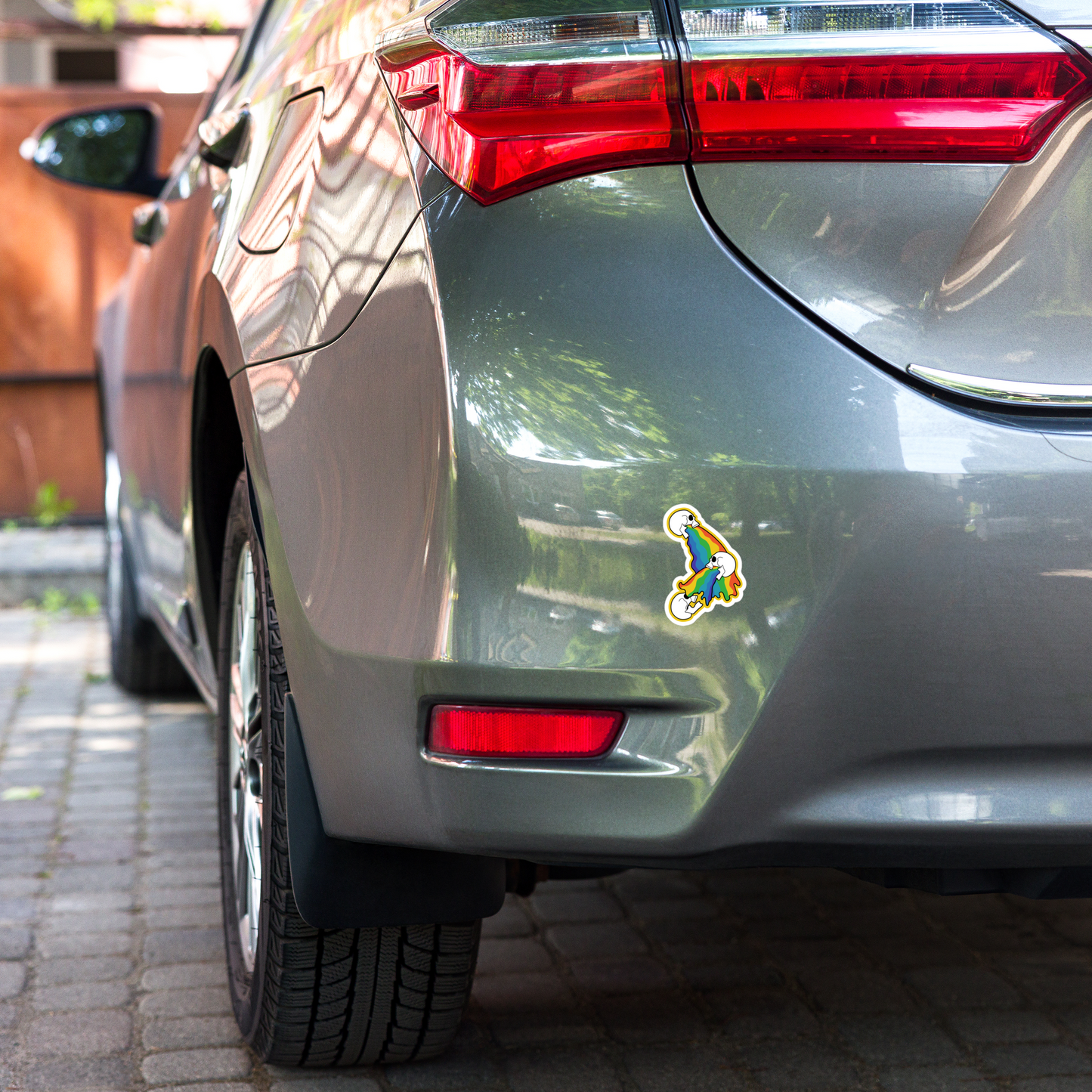 Car's rear end with a colorful rainbow vomit sticker on a brick road