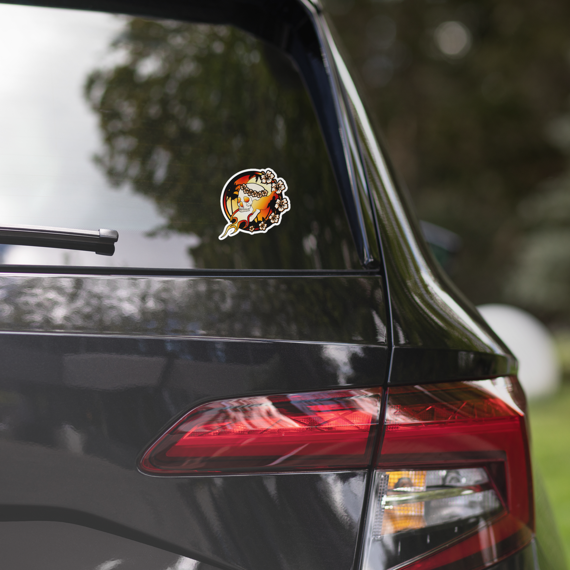 Car sticker of a skull with floral wreath and flames on a white background on a car's rear window with a blurred outdoor background