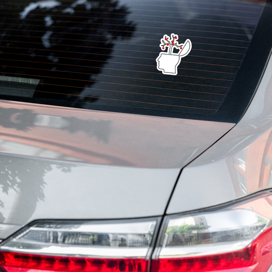 Car sticker of an outline of a head with an open brain featuring branches with red apples on a white background on a car's rear window.