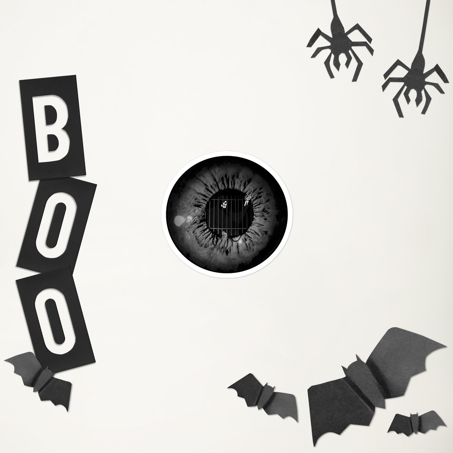 A black and white sticker of an eye with the grim reaper caged in the iris in a black metal style in front of Halloween-themed decorations including 'BOO' letters, and bats on a white background.