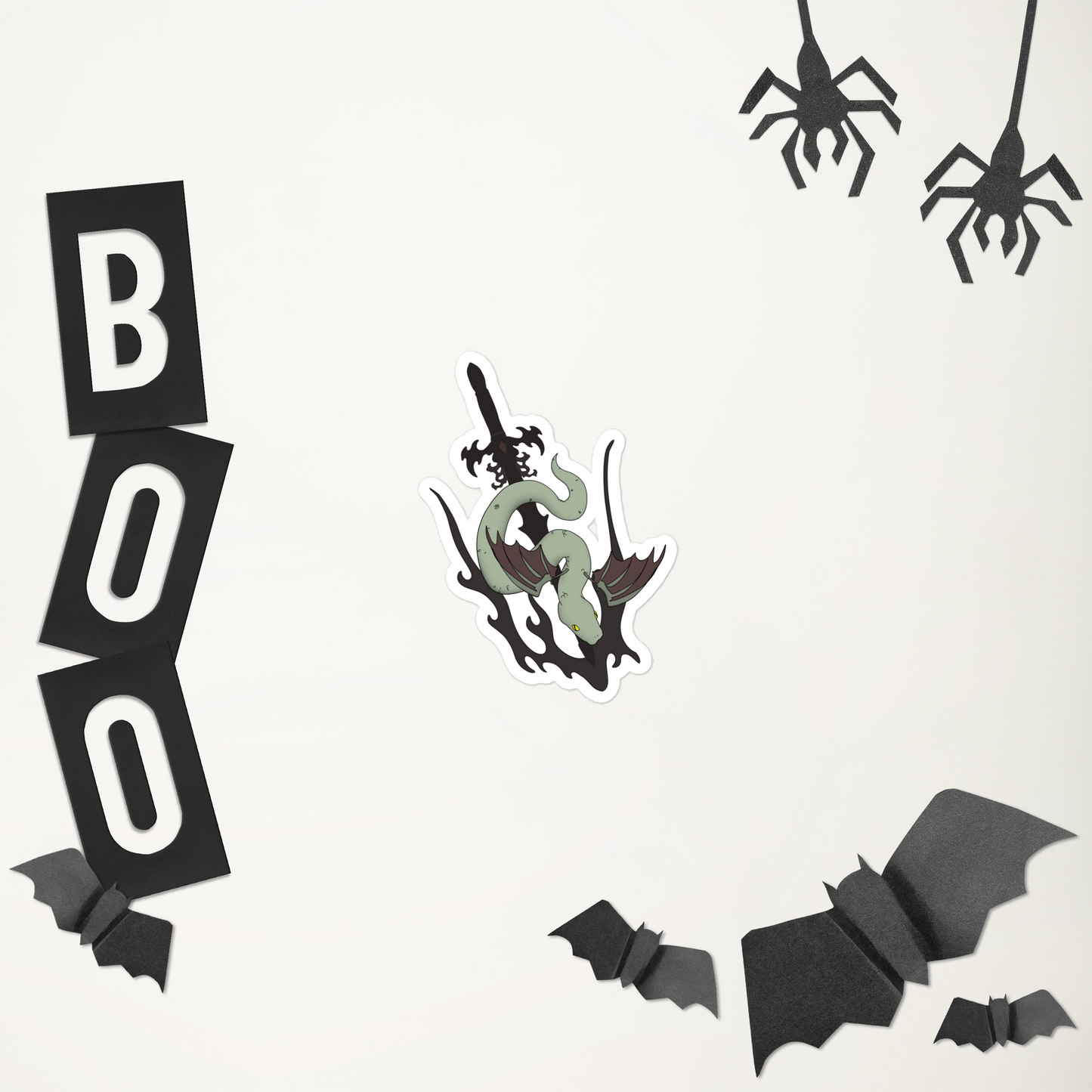 A die-cut vinyl sticker featuring a stylized green snake wrapped around a black sword, shown on a plain white background, including black paper spiders, bats, a black-and-white 'BOO' banner, and a ghost-shaped decoration with a green face and sword.