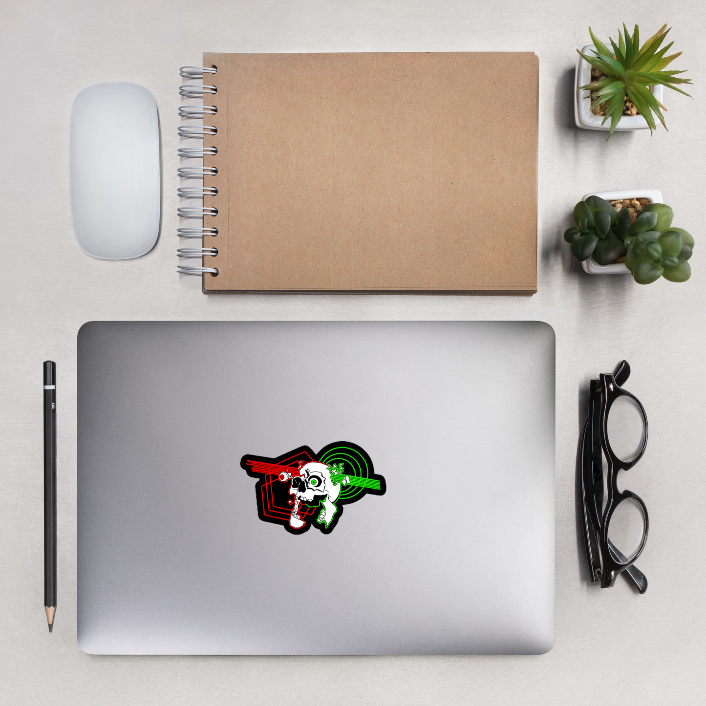 Laptop with a sticker on a desk with a notebook, mouse, pencil, and plants.