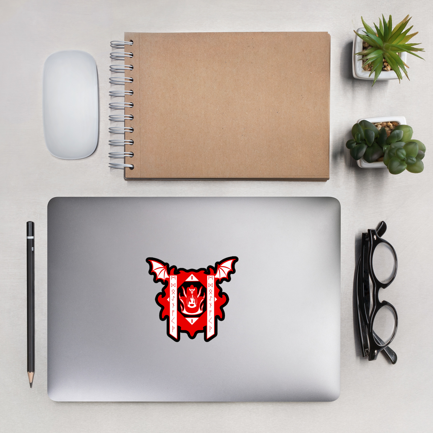 Laptop with a red and white design on a desk with a notebook, mouse, pencil, and glasses.