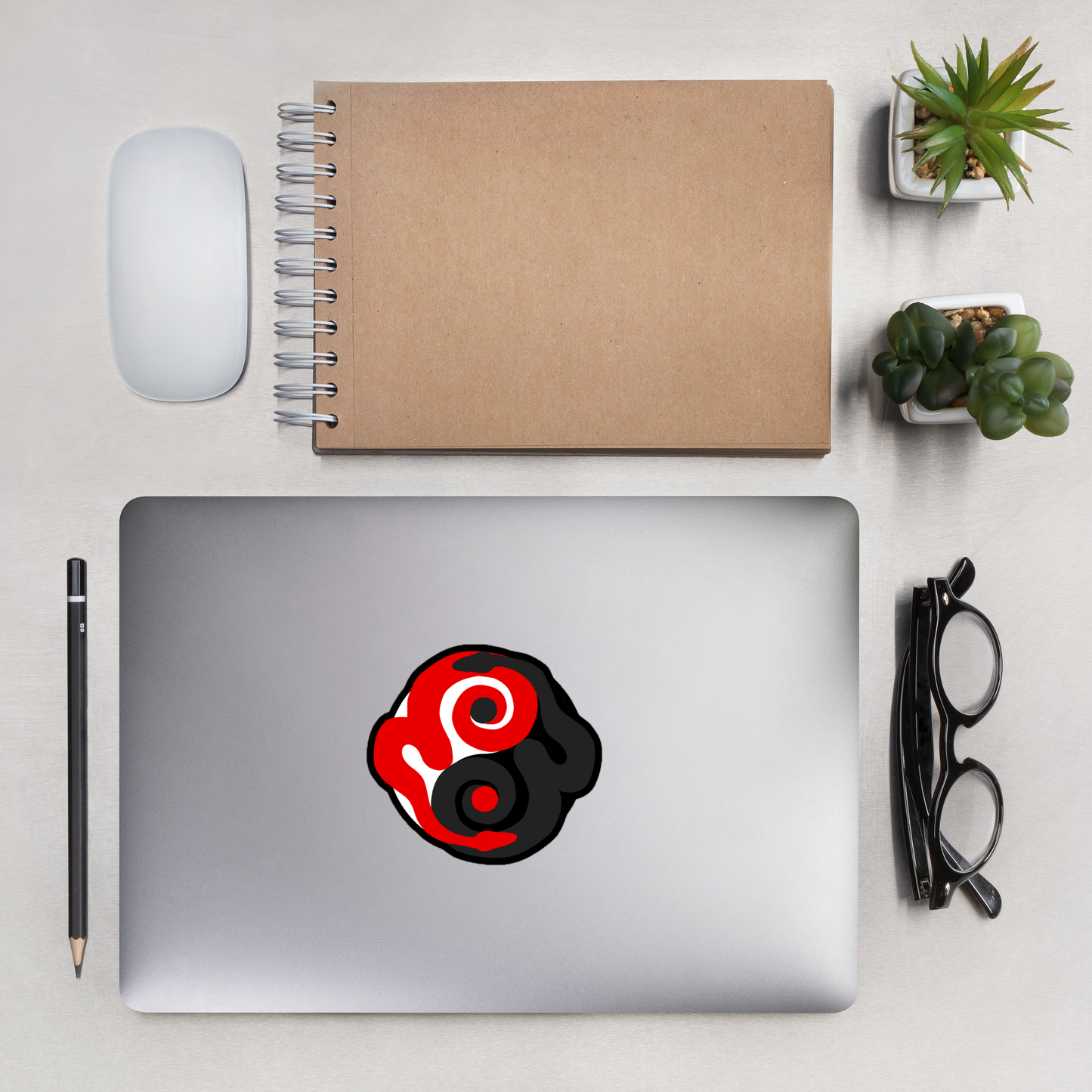 Laptop with a red and black logo on a desk with a notebook, mouse, and plants.