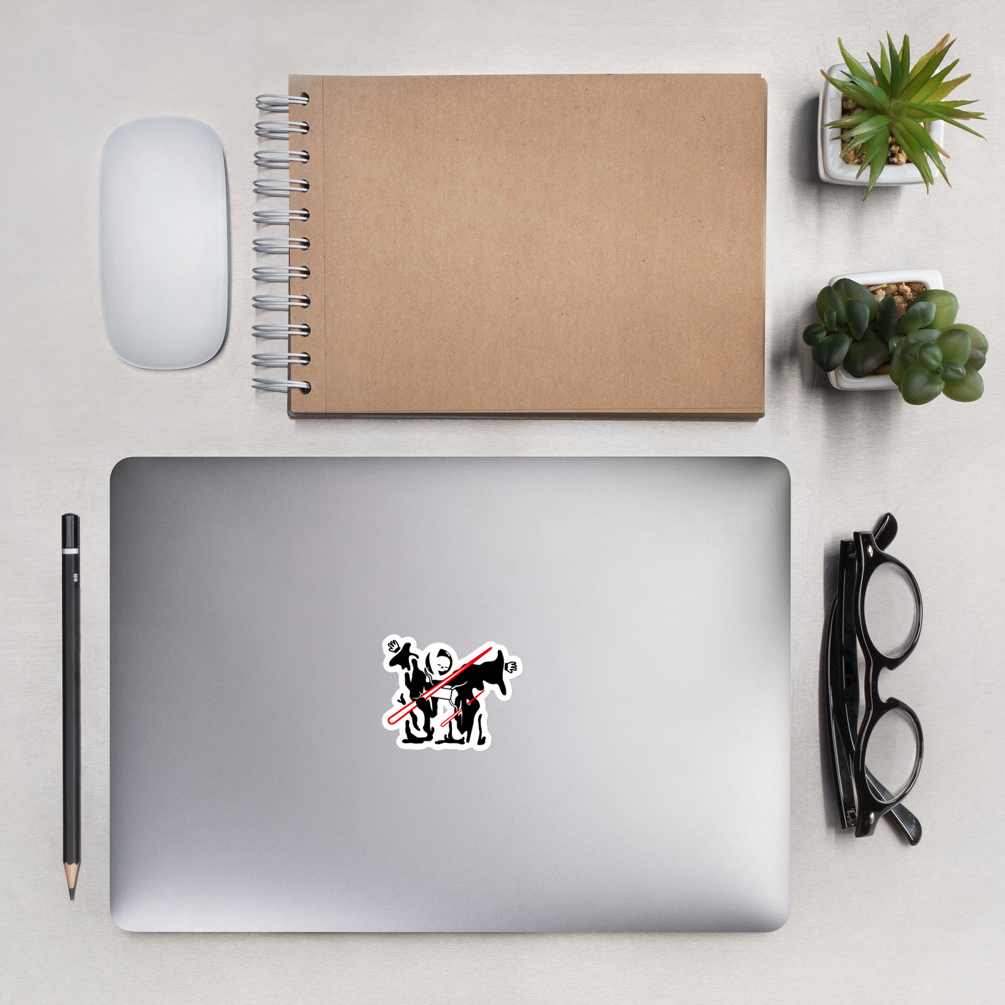 Laptop with a sticker of neorebellion mascot rob being pierced by a red laser on a white background on a desk with a notebook, mouse, pencil, and plants.