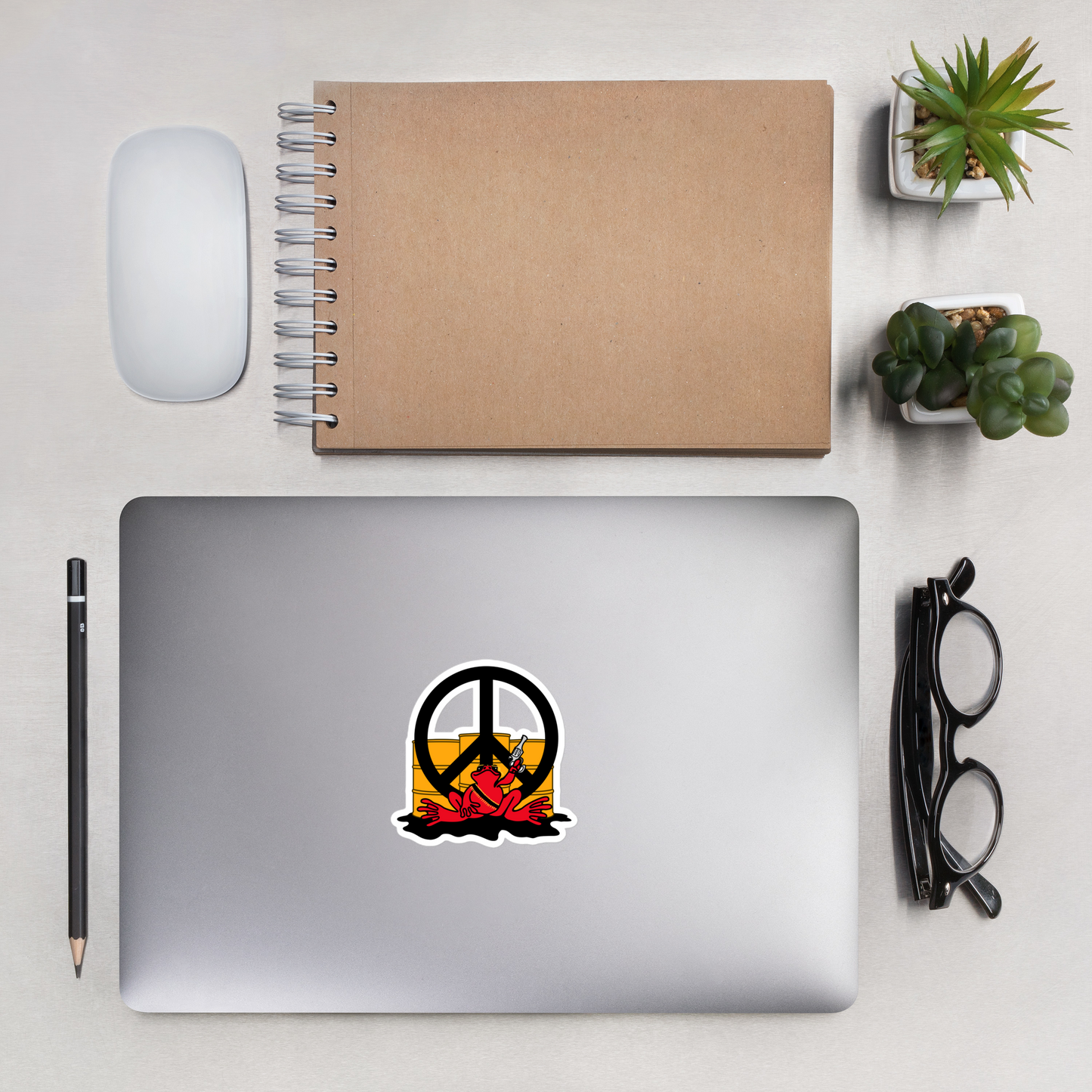 Laptop with a peace symbol and red frog design, surrounded by office supplies on a light surface.