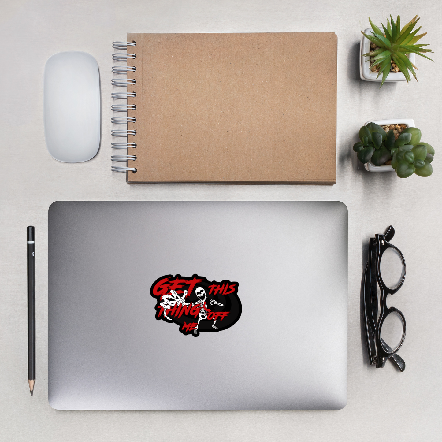 Laptop with a sticker on a desk with a notebook, mouse, pencil, and plants.