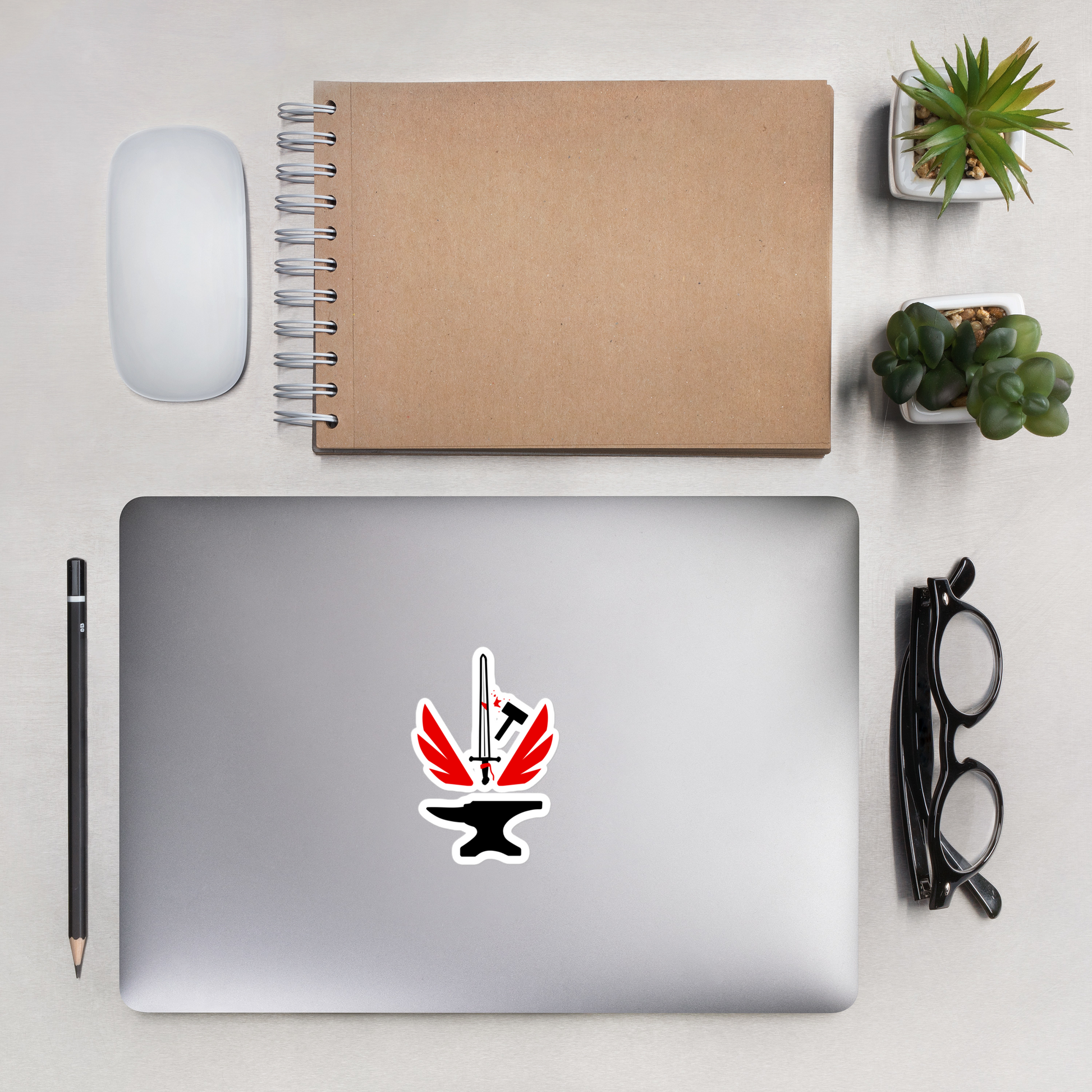 Laptop with a sticker on a desk with a notebook, mouse, pencil, and glasses.