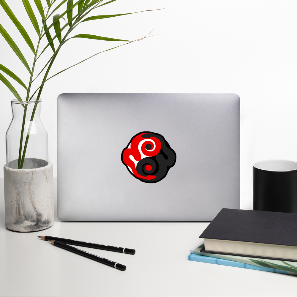 Laptop with a red and black circular design on a white surface with a plant, notebook, and cup.