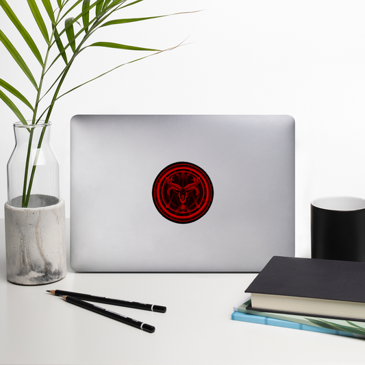 Laptop with a red and black circular sticker on a white surface with a plant, pencils, and books.
