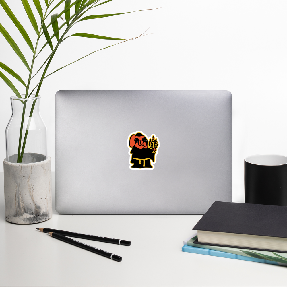 Laptop with a sticker of an orange cartoon dog in a black robe, and holding a candelabra on a white background on a desk with a plant, pencils, and books.