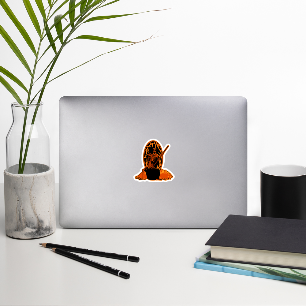 Laptop with a skeletal figure with a staff and cauldron on an orange and black background sticker on a desk with a plant, pencils, and books.