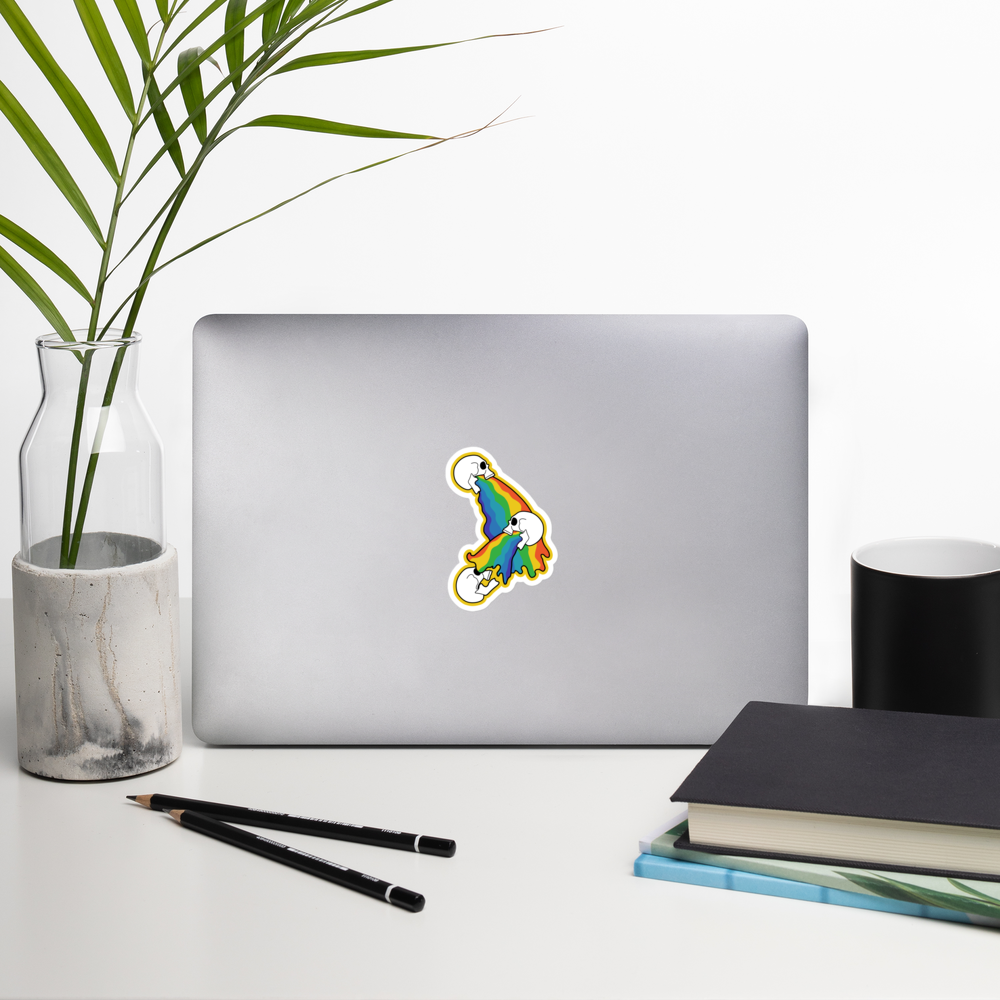 Laptop with a colorful rainbow vomit sticker on a desk with a plant, pencils, and books.