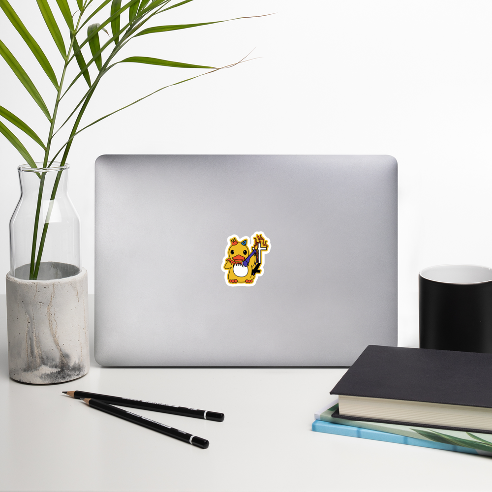 Laptop with a sticker of colorful duck holding a flaming candle in front of a cross grave on a desk with a plant, pencils, and books.