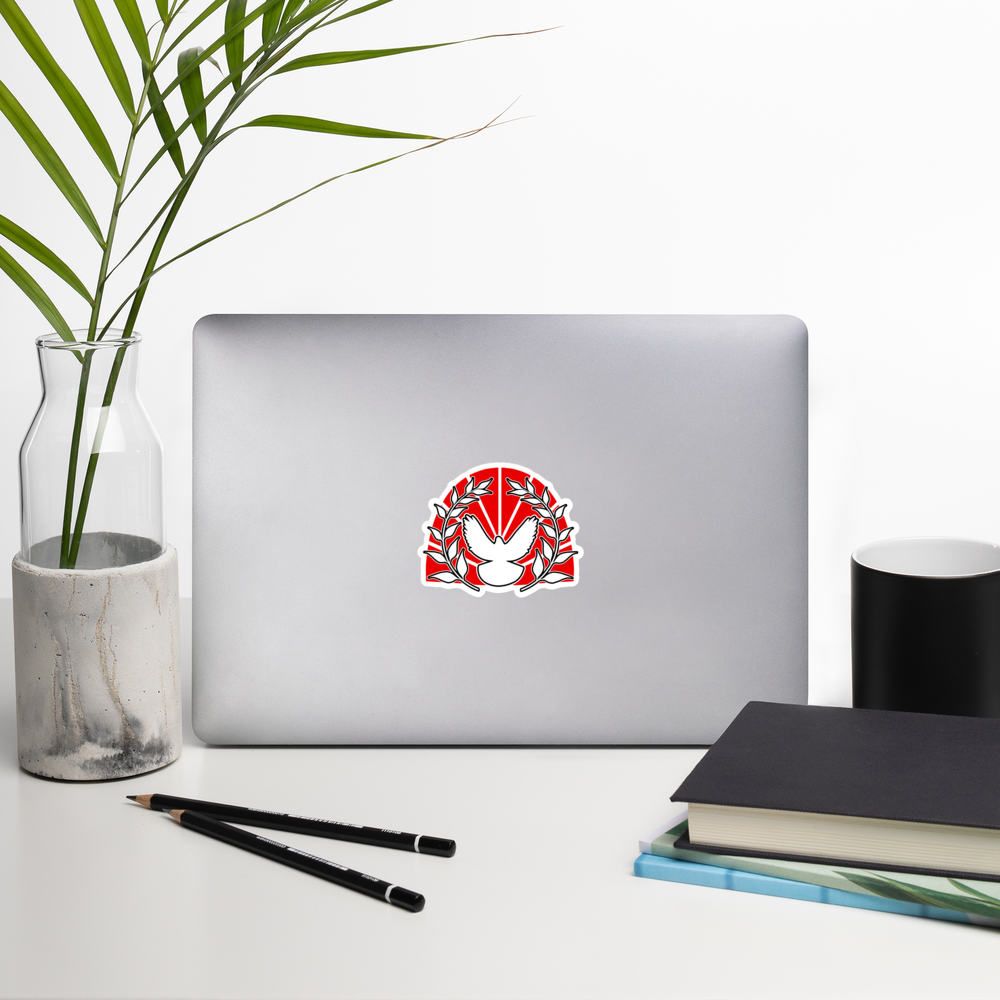 Laptop with a red and white peace dove emblem sticker on a white surface with a plant, pencils, and books.