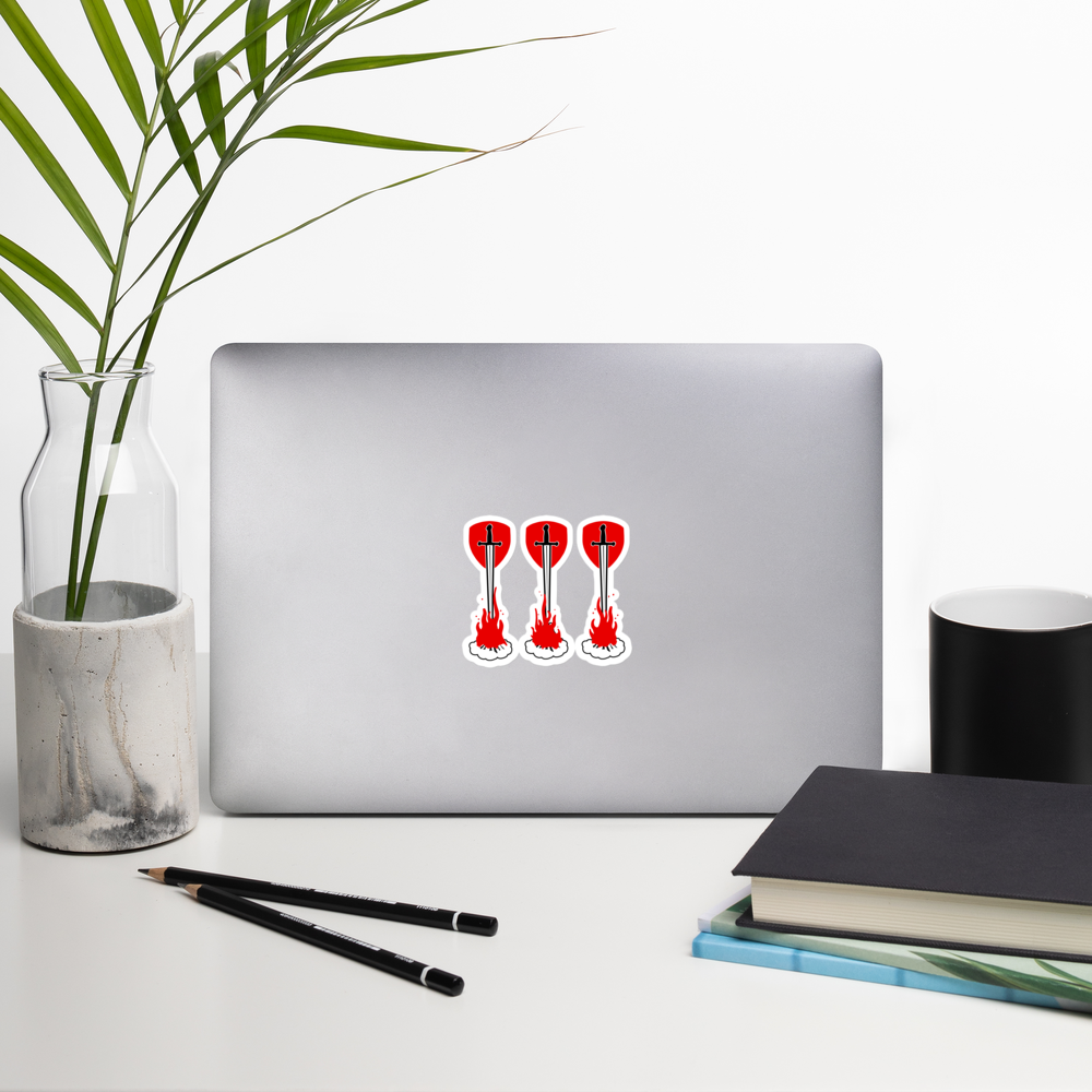 Laptop with a sticker of three swords over fire in front of shields in a red and white design on a white surface with a plant, pencils, and books.