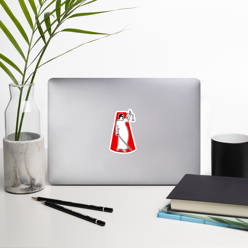 Laptop with a sticker of a lady justice figure holding a sword and scale on a red background a desk with a plant, pencils, and books.