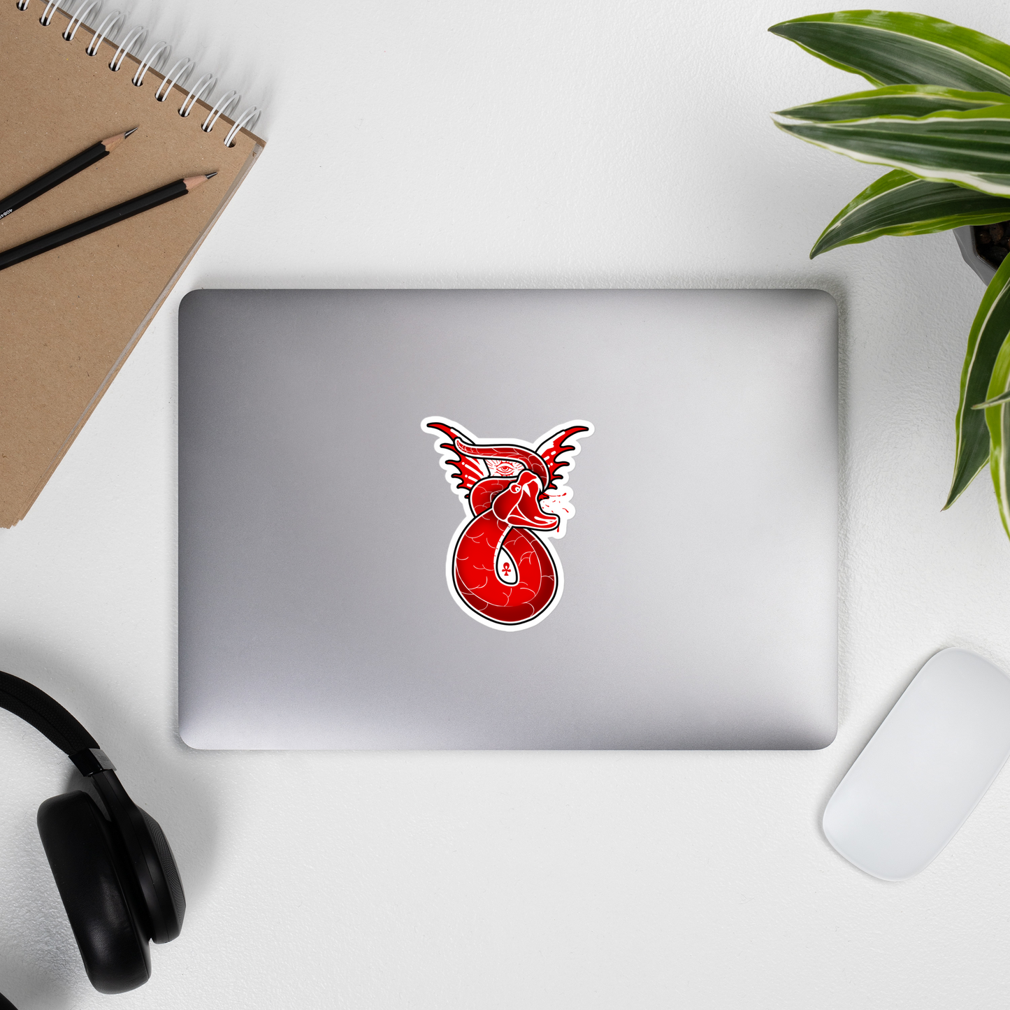 Laptop with a red snake logo on a white surface with a notebook, pencils, and headphones.