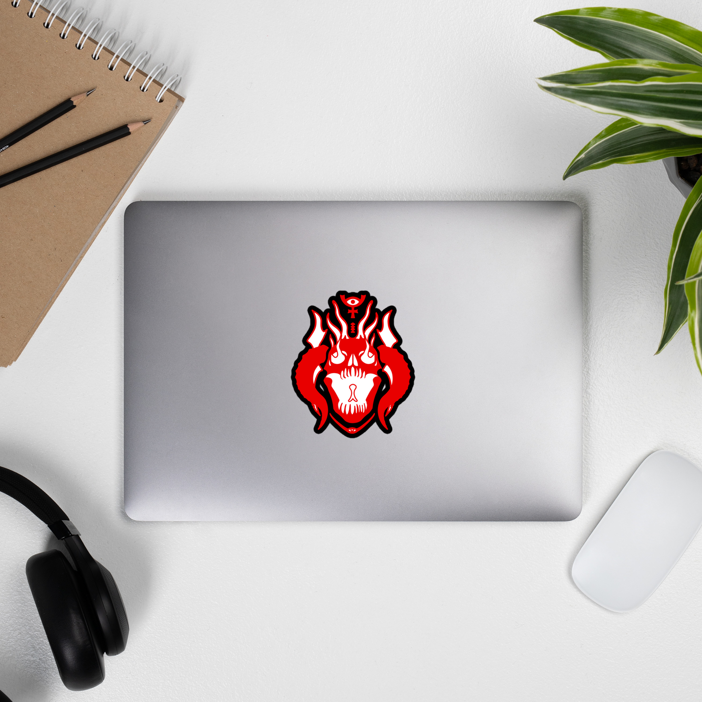 Laptop with a red and black emblem on a white surface with a notebook, pencils, and headphones.