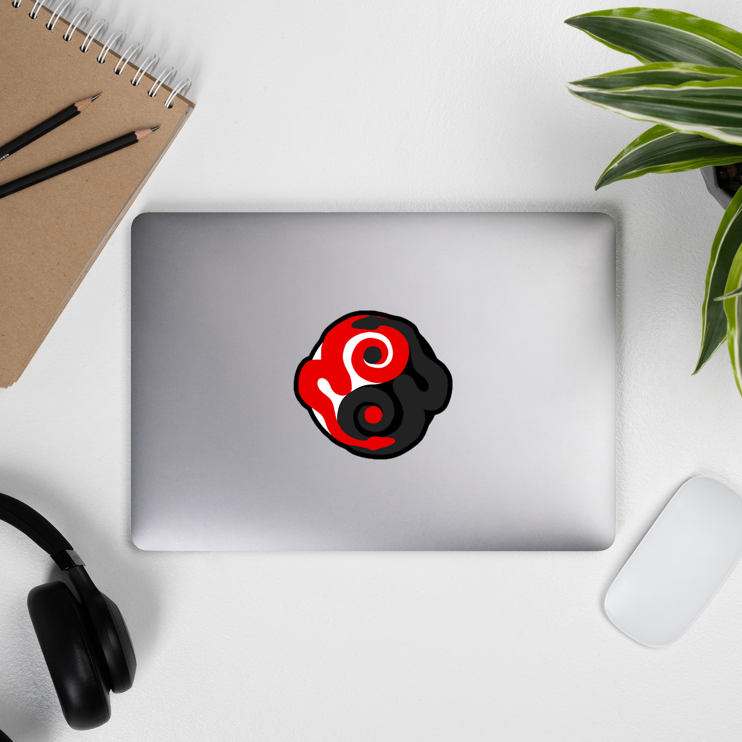 Laptop with a red and black logo on a white surface with a notebook, pencils, and plant.