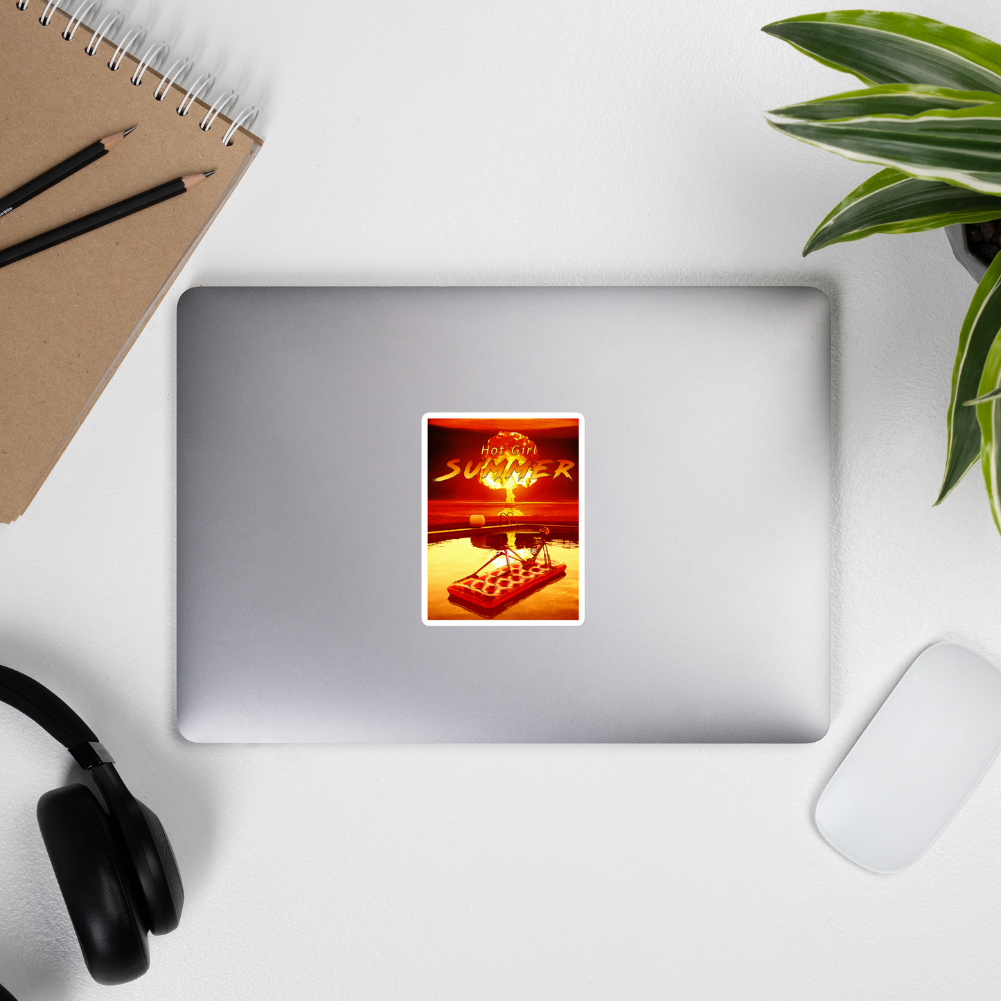 Laptop with a 'Hot Girl Summer' movie poster sticker on a desk with a notebook, pens, and headphones.