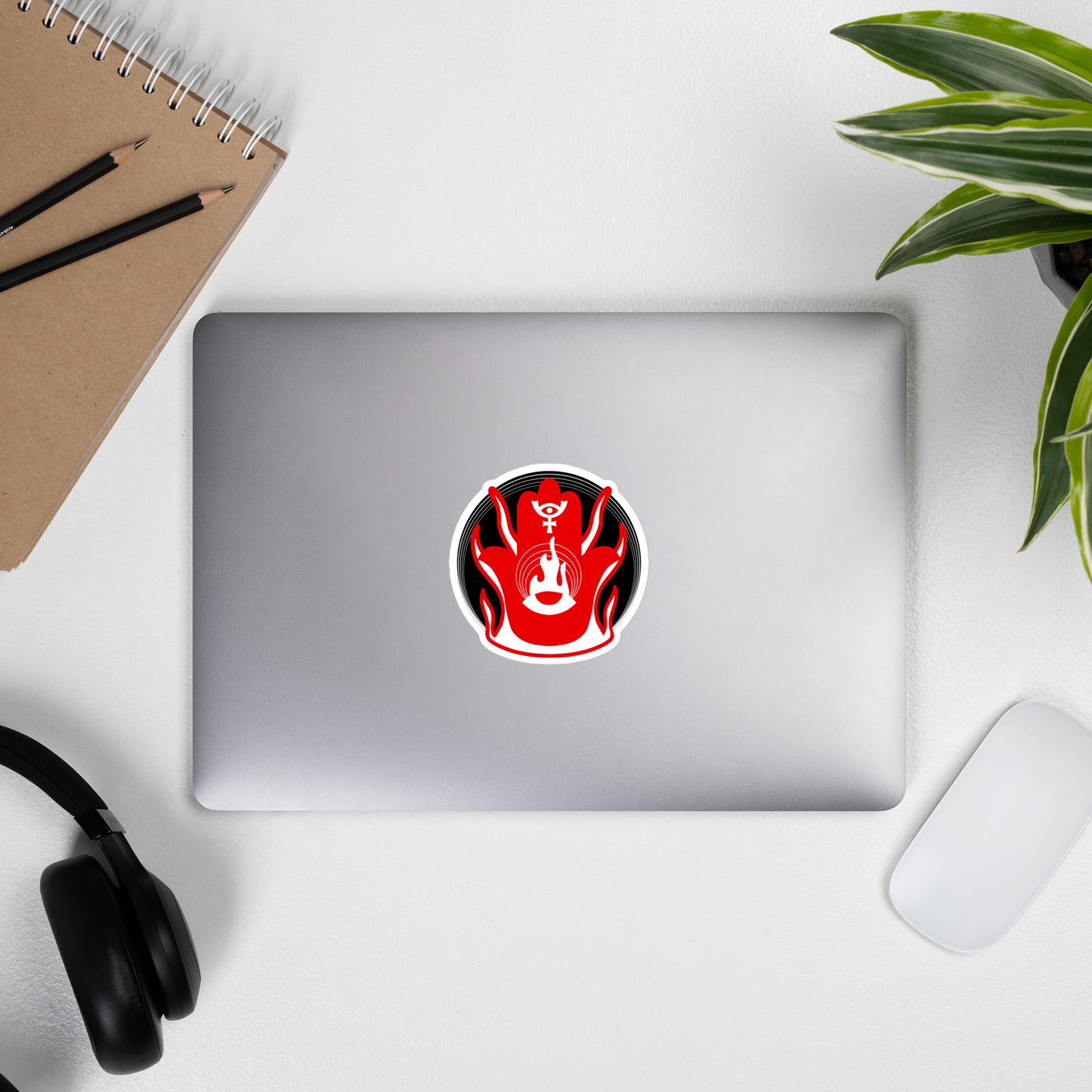 Laptop with a red and black sticker on a desk with a notebook, pens, and headphones.