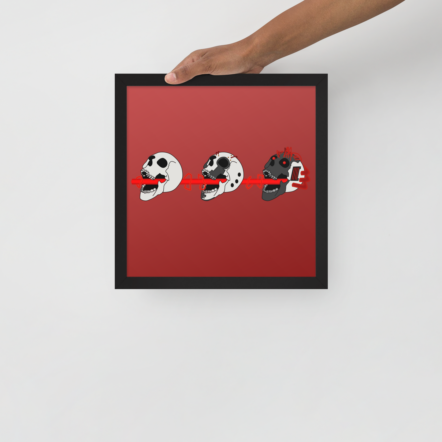 Framed artwork with three cartoon-like cyberpunk skull illustrations on a red background, held by a hand.