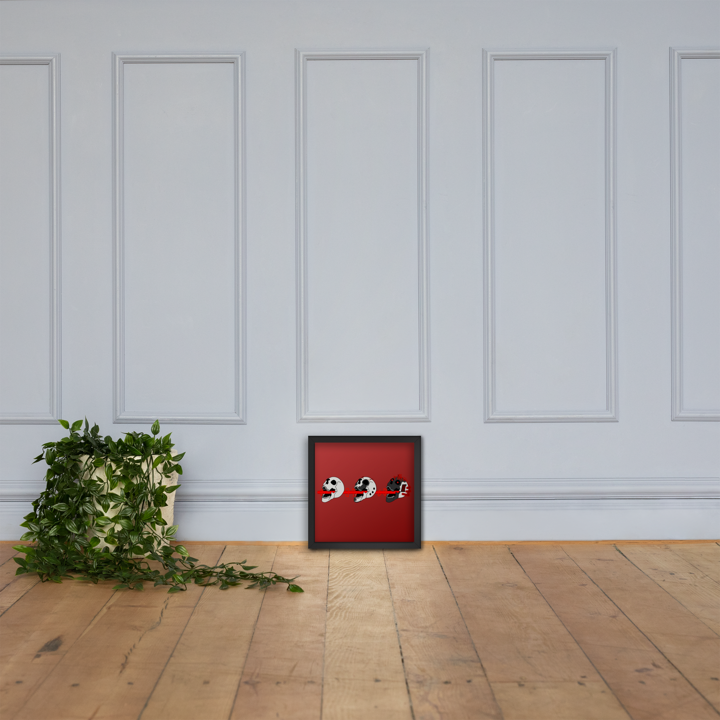 Framed red cyberpunk artwork with three skulls on a wooden floor with a white paneled wall background