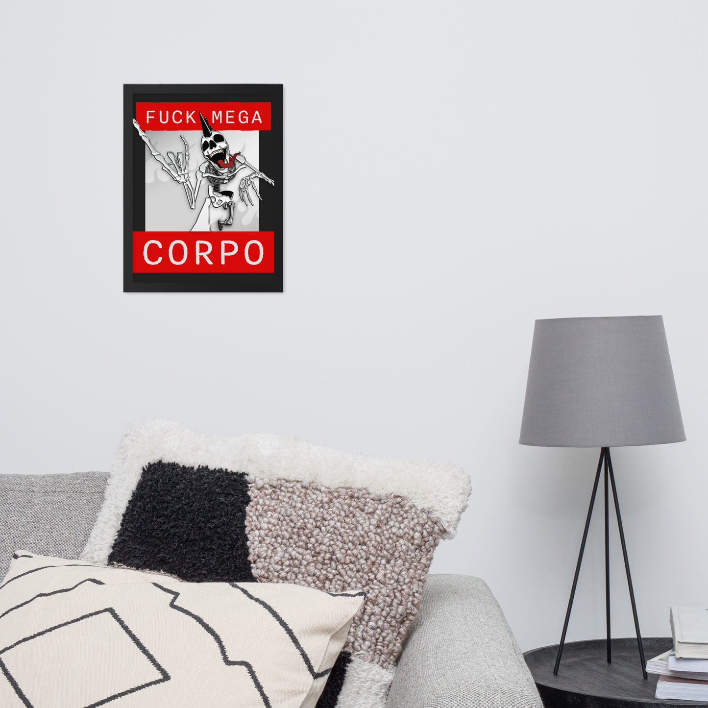 Framed artwork of a heavy metal skeleton in front of 'FUCK MEGA CORPO' text with red, white, black, and grey coloration above a sofa with decorative pillows and a lamp.