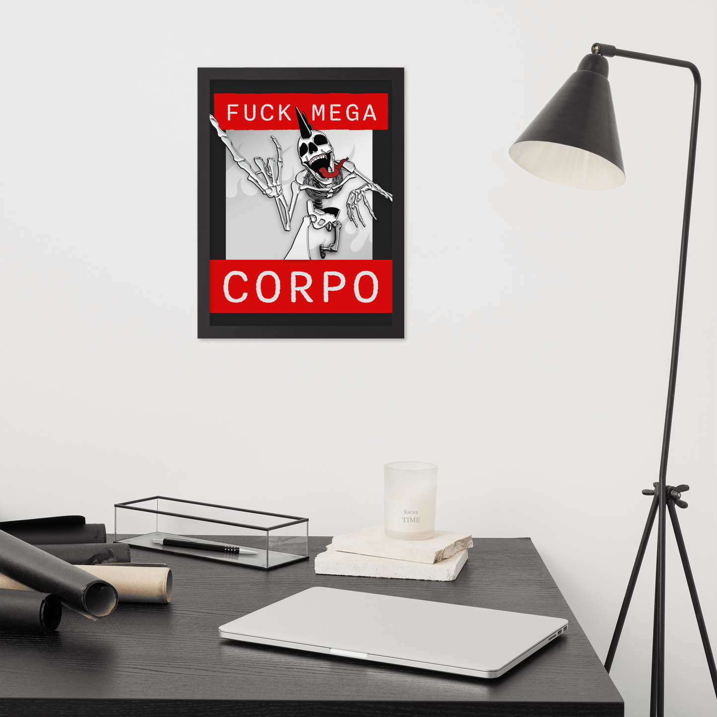 Framed artwork of a heavy metal skeleton in front of 'FUCK MEGA CORPO' text with red, white, black, and grey coloration on a wall above a desk with office supplies.