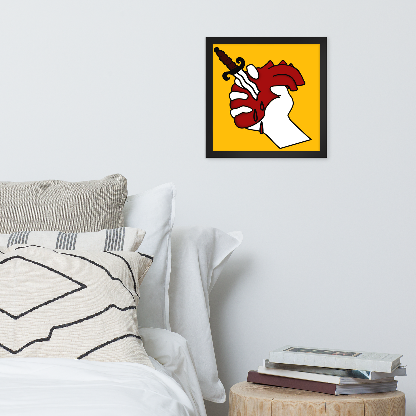 Framed tattoo style heart stab artwork above a bed with pillows and books on a nightstand.