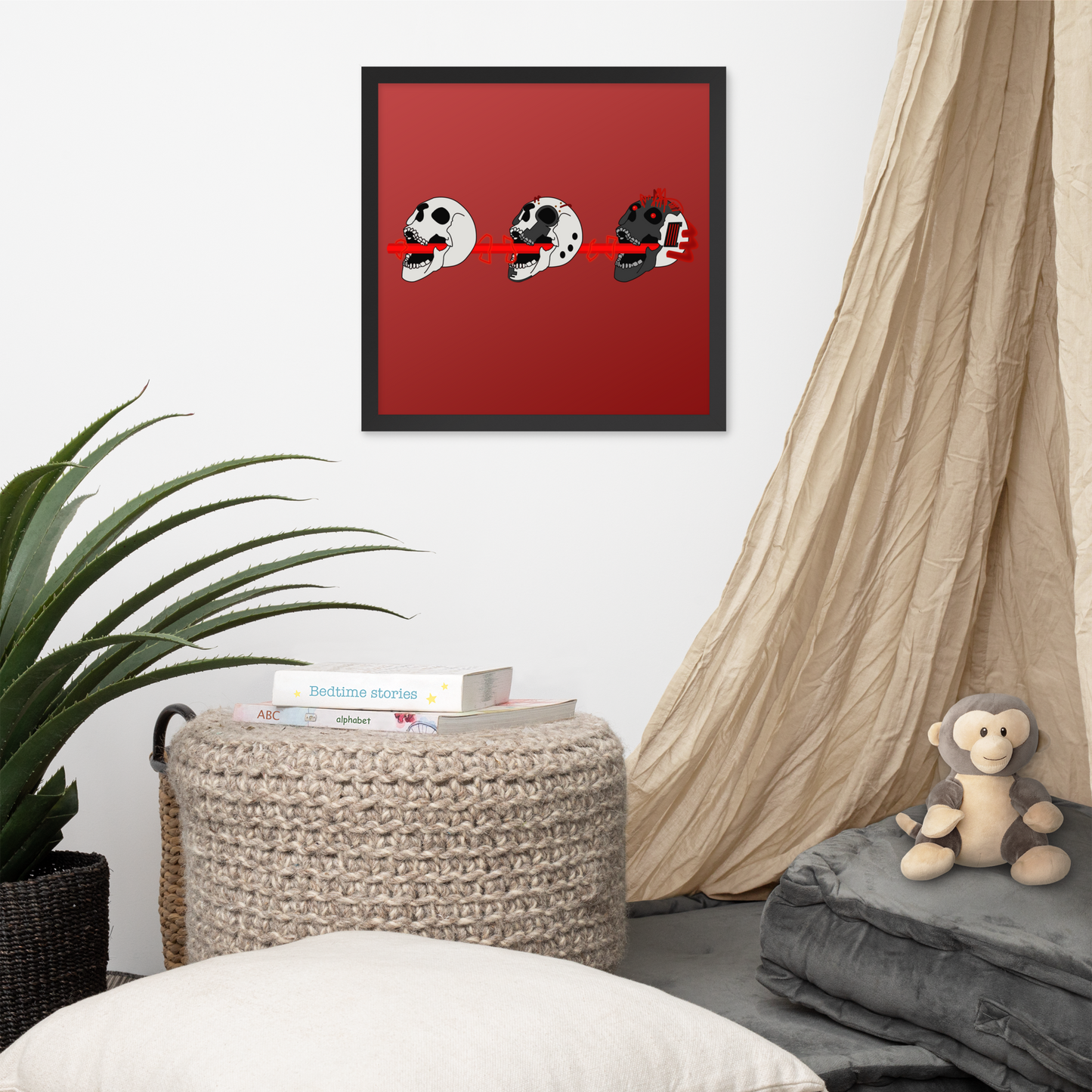 Framed artwork with 3 cyberpunk skullson a red background in a room with a plant, ottoman, and monkey plush toy.