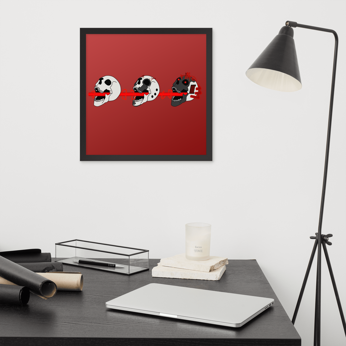 Framed artwork with skulls shooting lasers in a cyberpunk style on a red background above a desk with a laptop and lamp.
