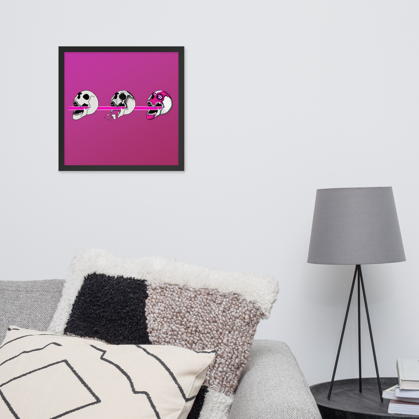 Framed 16x16 artwork of a pink background and three stylized cyberpunk skull designs shooting a laser with purple and black details in a living room setting.
